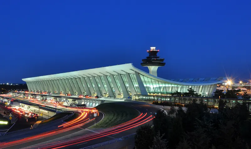 An airport terminal at dusk with light trails from passing cars
