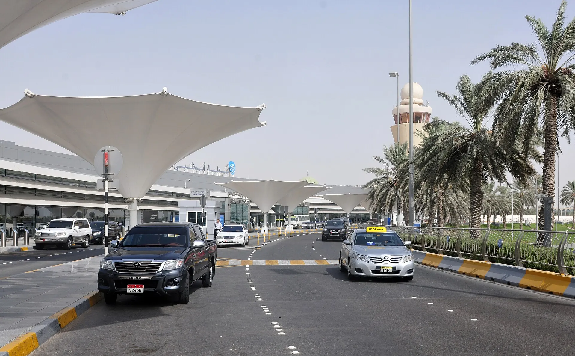 Cars and taxis on the palm-lined road outside an airport terminal